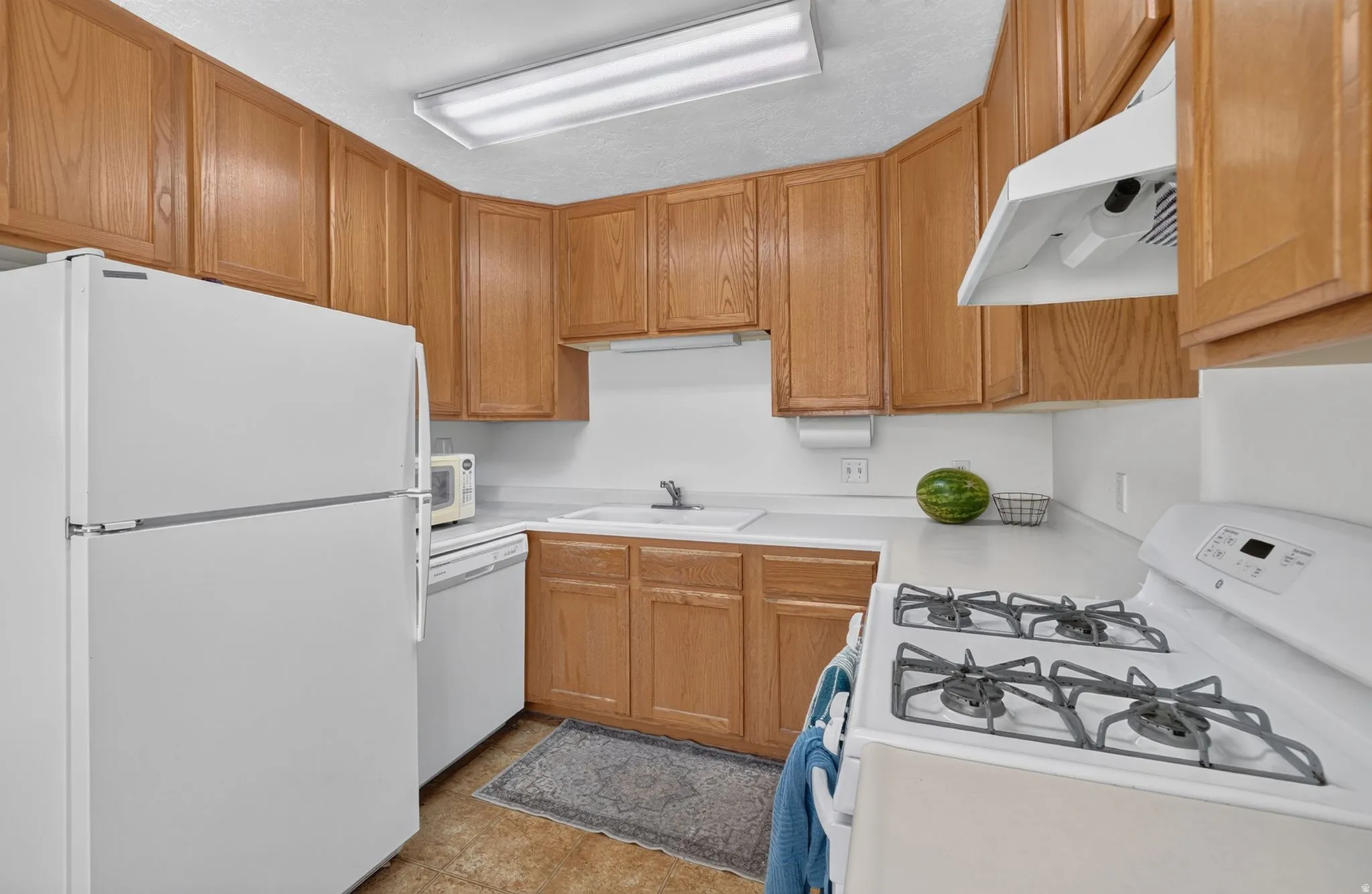 Kitchen featuring wood-finish cabinetry, white countertops, a white gas range, and a white refrigerator