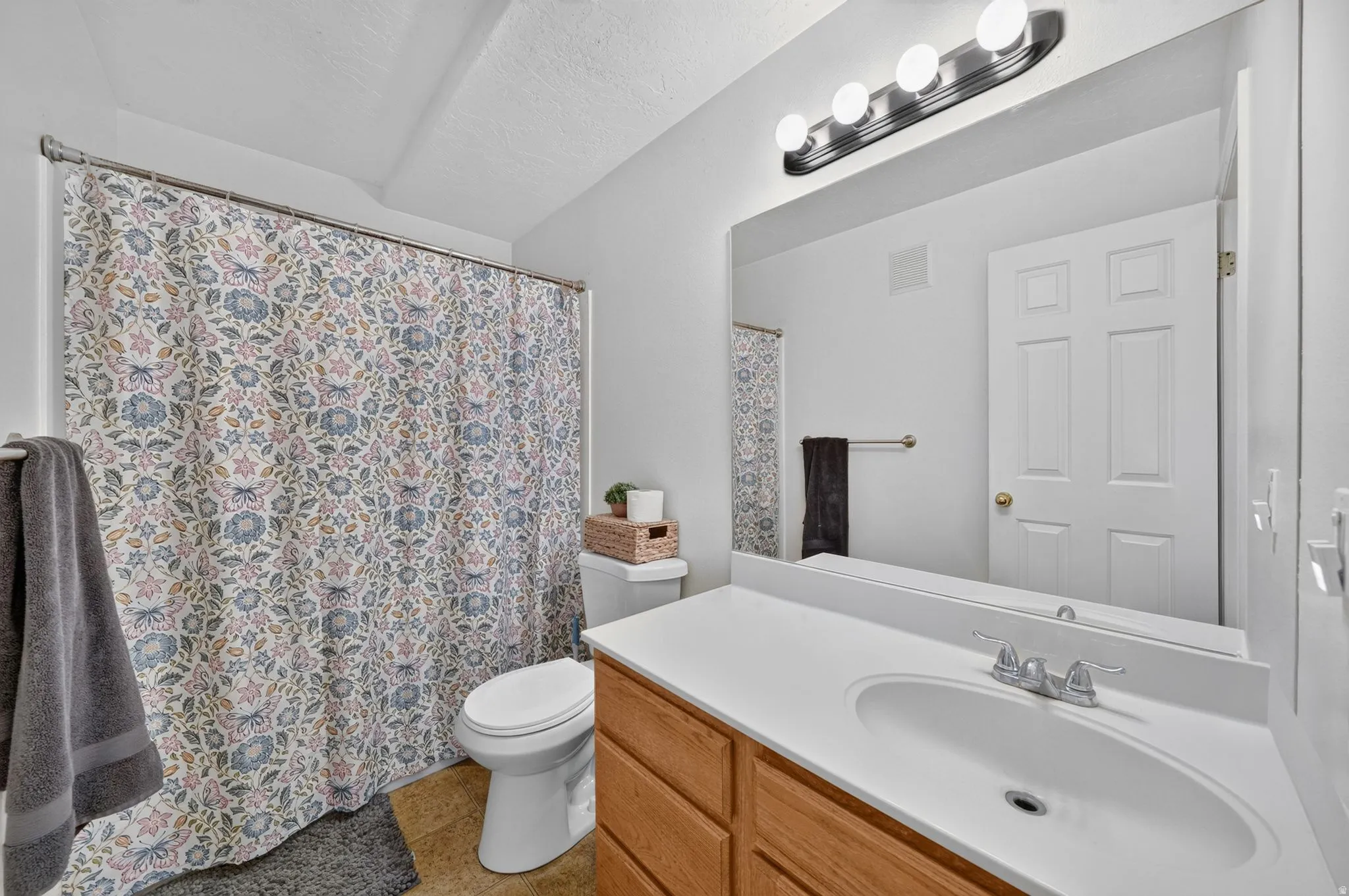 Bathroom featuring a single vanity with a white countertop and light wood-finish cabinetry, a large wall-mounted mirror, brushed nickel light fixture, and a toilet