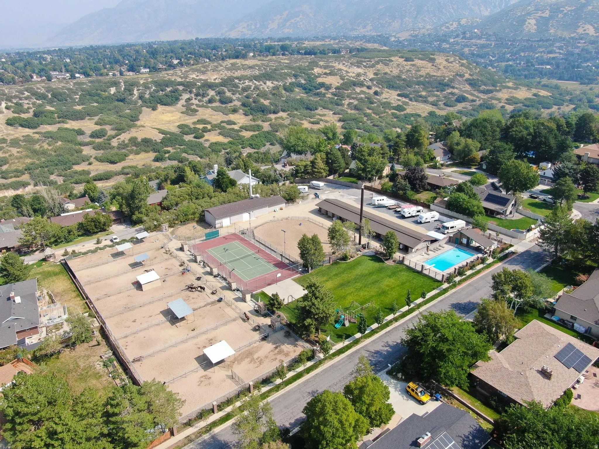 Expansive property featuring multiple equestrian paddocks with shelters, a full-size tennis court, a swimming pool with surrounding deck, and a manicured lawn area