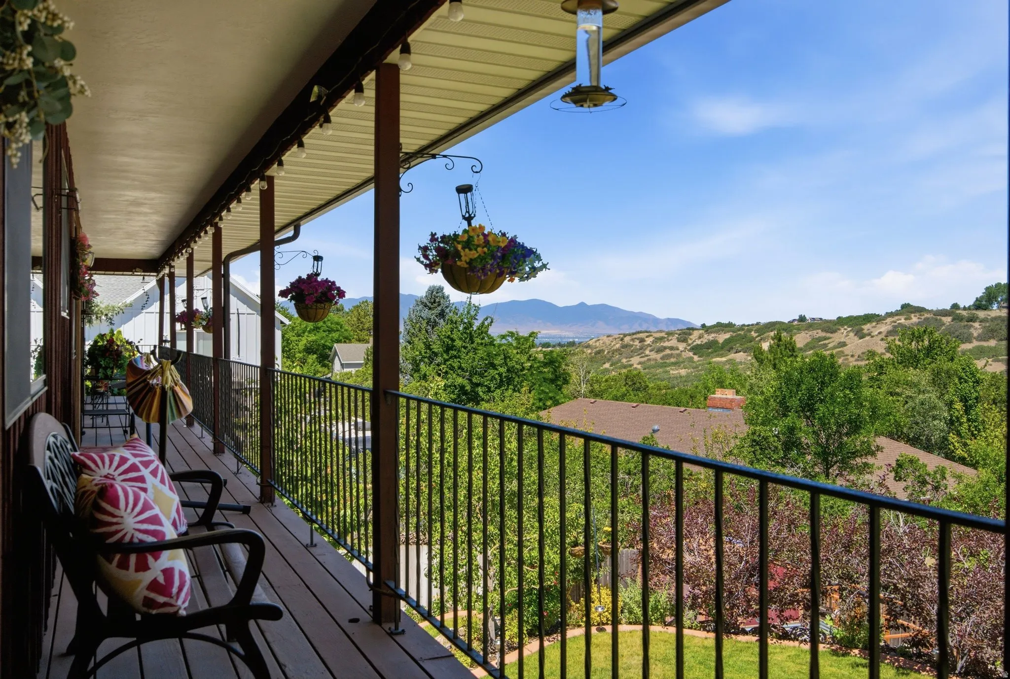 Spacious outdoor balcony featuring a dark wood-finish deck, black metal railing, and a slatted ceiling with integrated string lighting