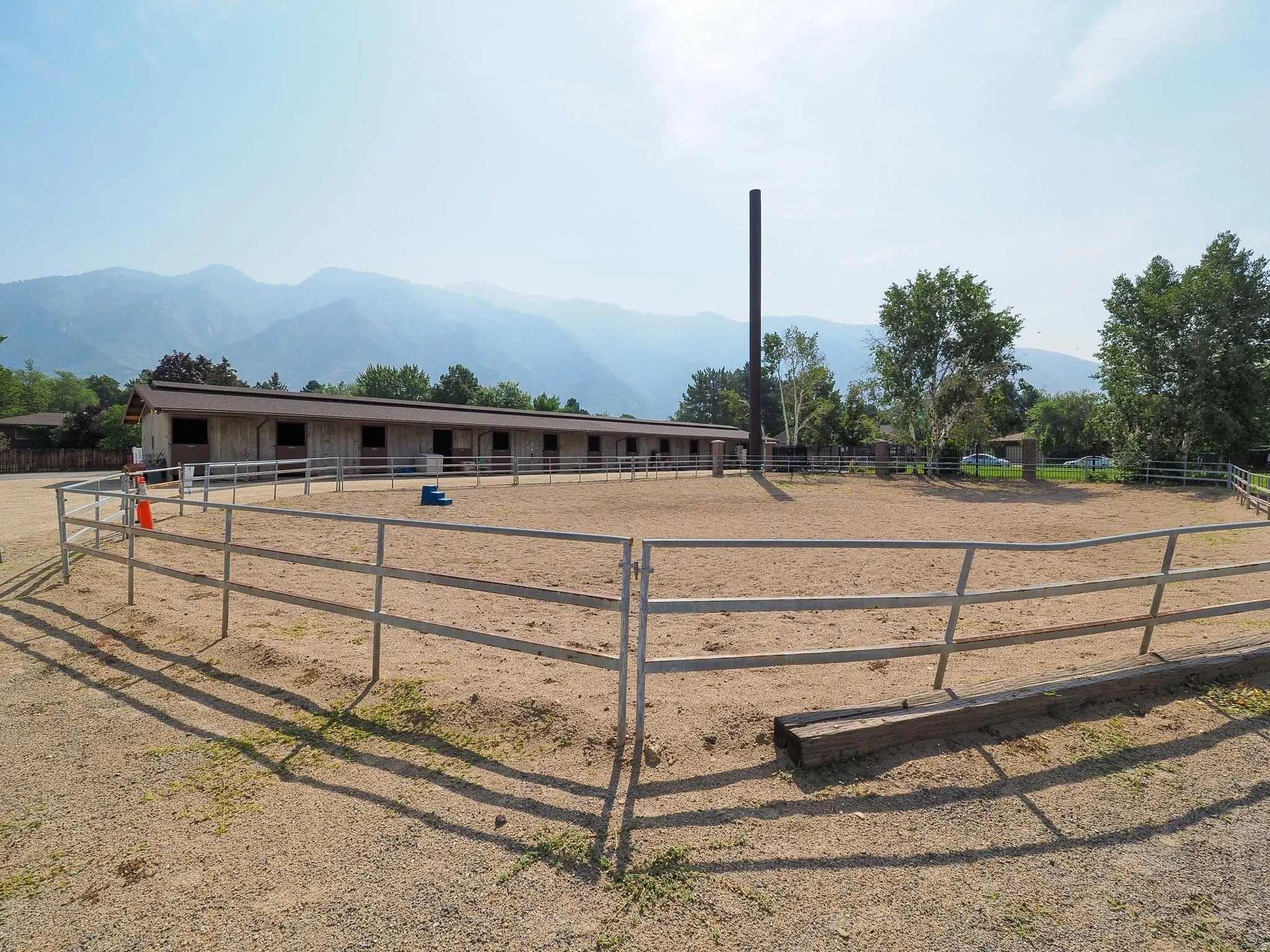Outdoor riding arena with sand footing, complemented by a multi-stall barn featuring individual openings