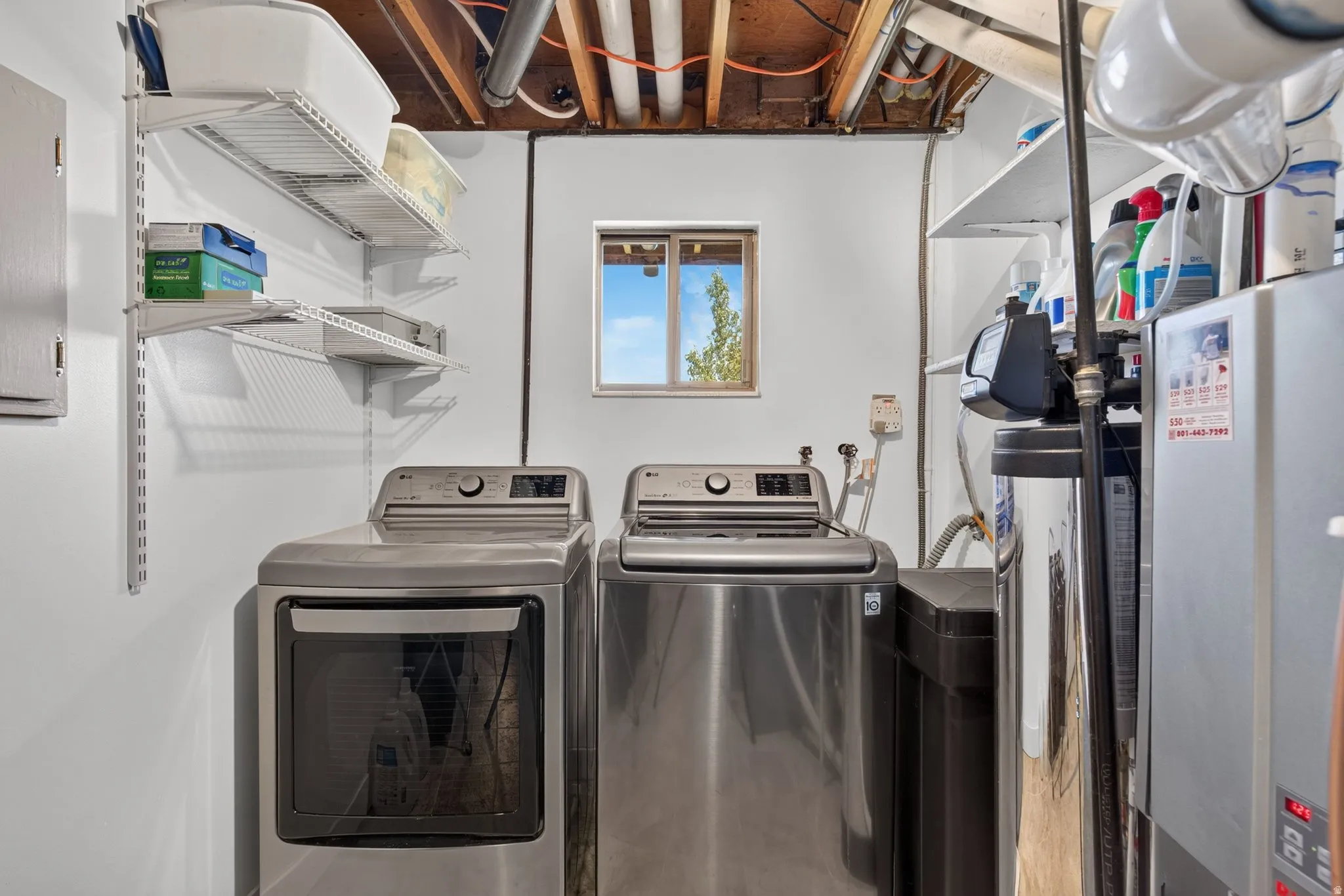 Dedicated utility area featuring a washer and dryer set, adjustable wall-mounted shelving, a water filtration system, and exposed ceiling joists
