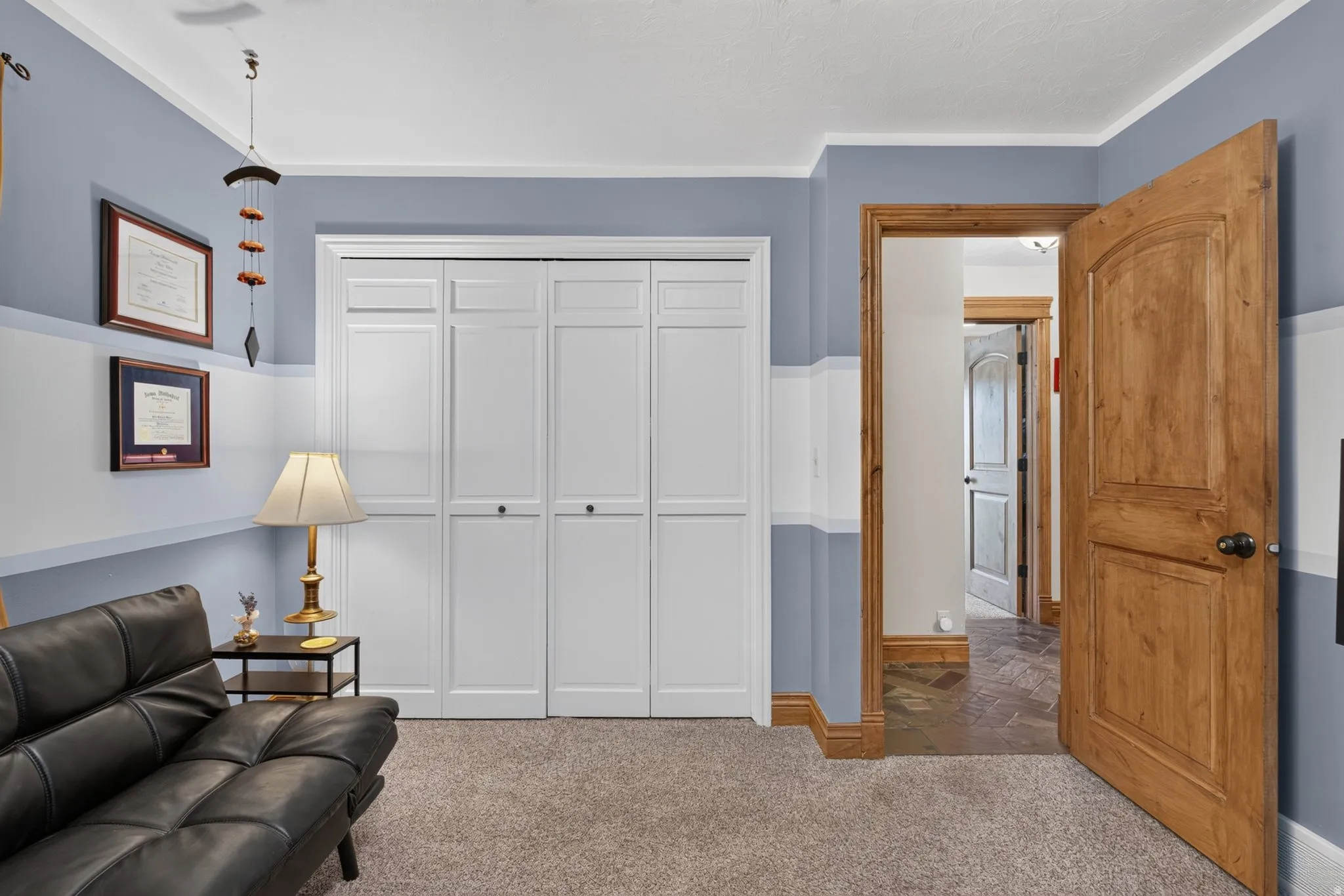 Carpeted room featuring a white bi-fold closet, natural wood door with black hardware, white baseboards, and two-tone wall paint