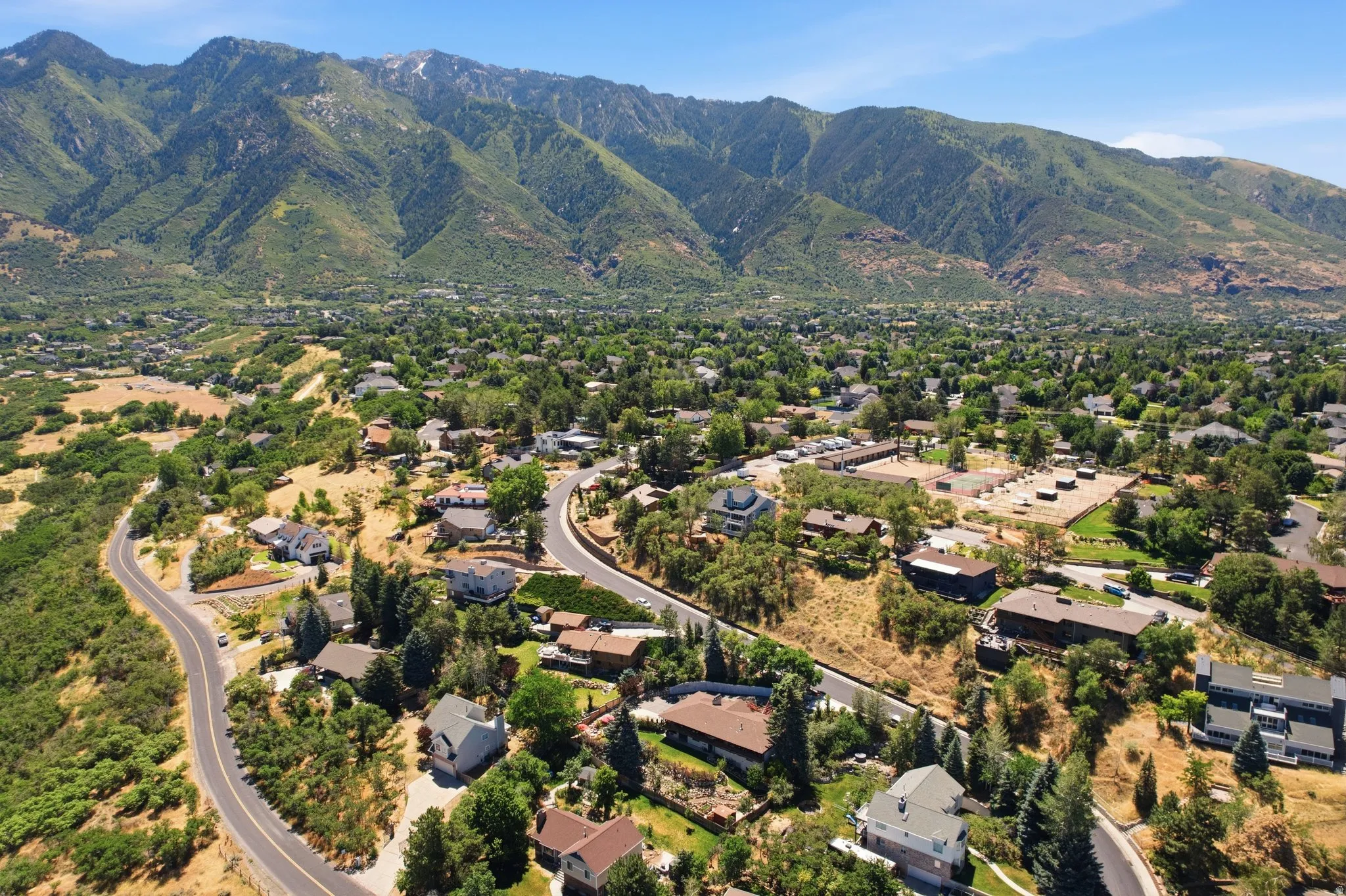 Expansive mountain backdrop with a residential area featuring numerous homes, mature trees, and paved roadways