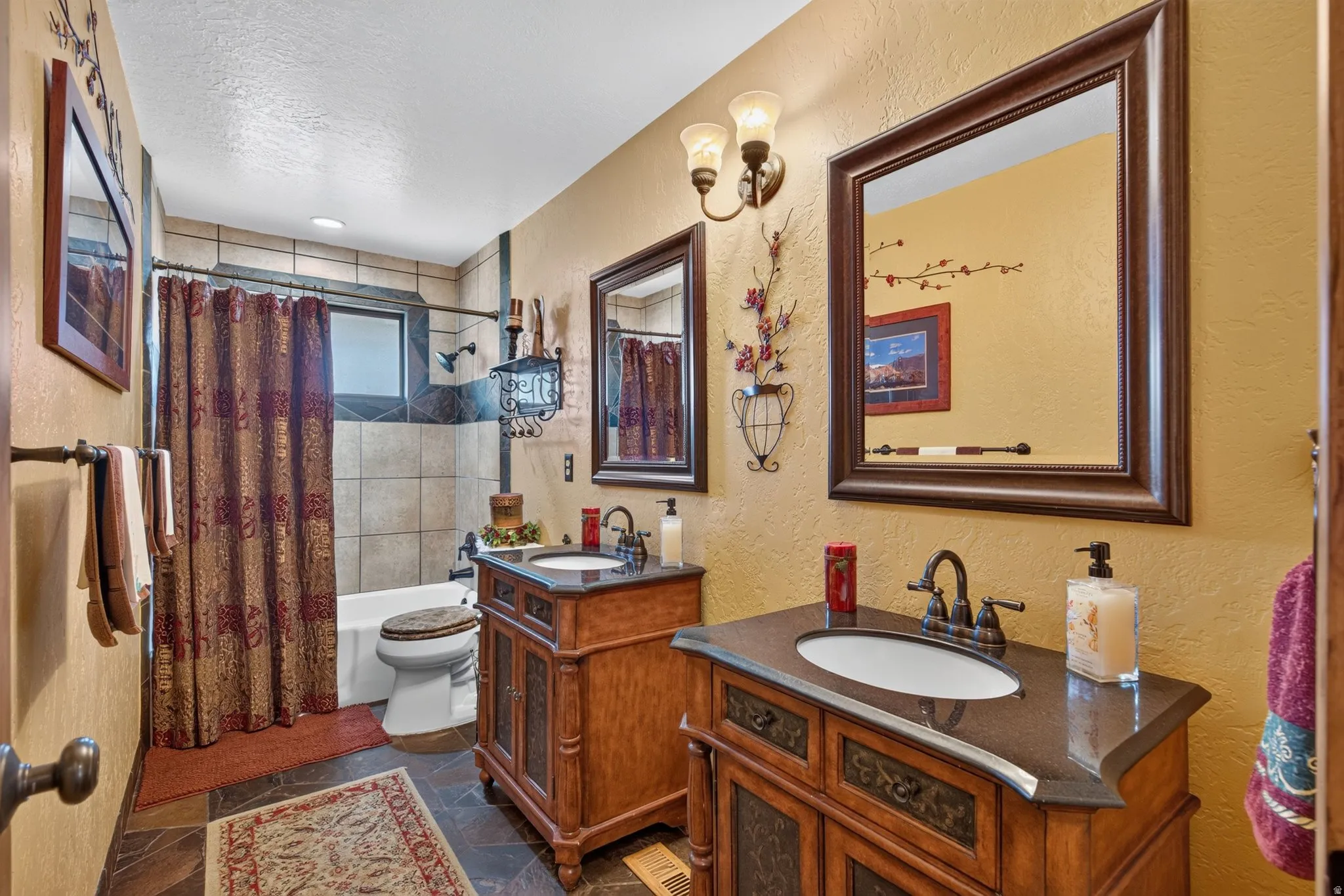 Bathroom featuring dual wood-finish vanities with dark countertops, a bathtub with tile surround, and tile flooring