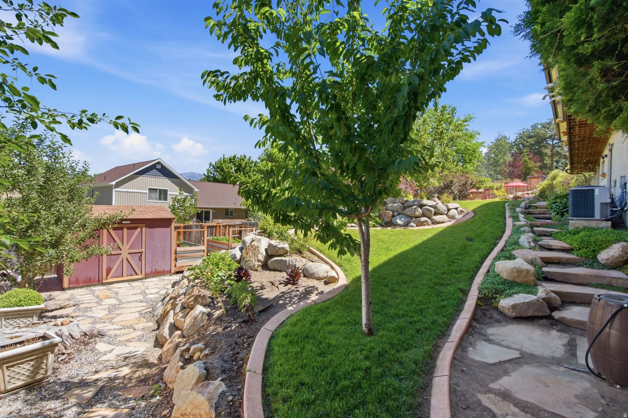 Expansive backyard featuring a stone pathway, terraced landscaping with rock retaining walls, and a dedicated storage shed