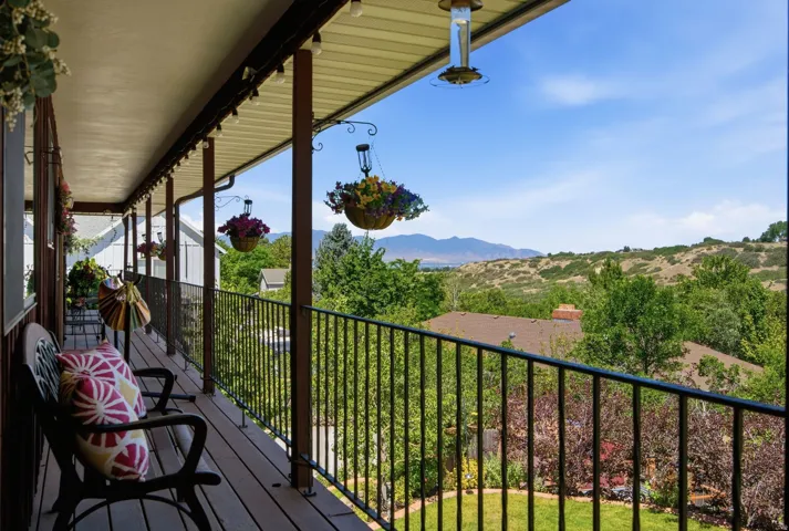 Spacious outdoor balcony featuring a dark wood-finish deck, black metal railing, and a slatted ceiling with integrated string lighting