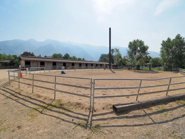 Outdoor riding arena with sand footing, complemented by a multi-stall barn featuring individual openings