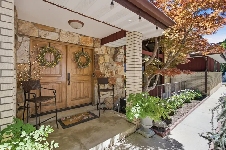 Stone and brick exterior featuring double wood-finish entry doors, an overhead soffit with recessed lighting, and a mature tree with vibrant foliage