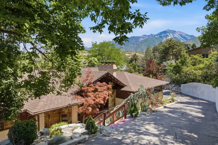 Multi-level residence featuring a brown shingle roof, stone and brick exterior, and a wooden deck railing