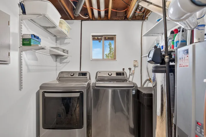 Dedicated utility area featuring a washer and dryer set, adjustable wall-mounted shelving, a water filtration system, and exposed ceiling joists