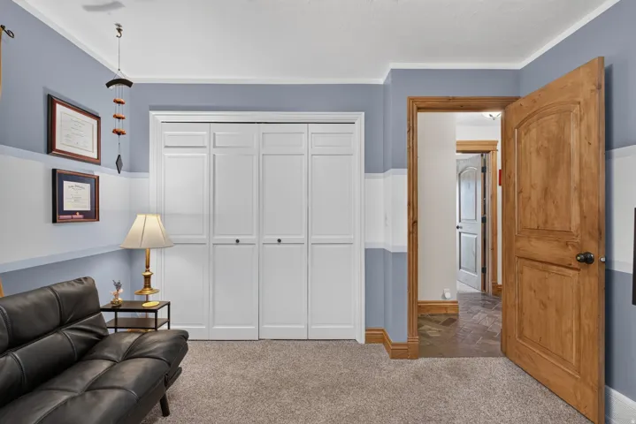 Carpeted room featuring a white bi-fold closet, natural wood door with black hardware, white baseboards, and two-tone wall paint