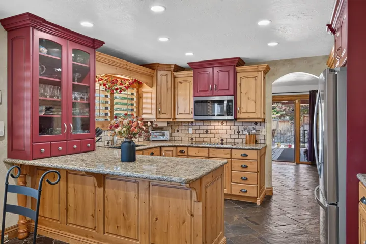 Kitchen featuring a large central island with granite countertop, wood cabinetry, subway tile backsplash, and stainless steel appliances