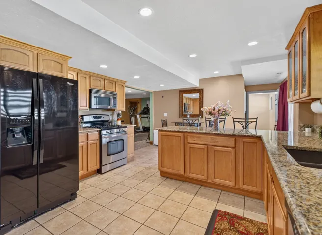 Kitchen featuring light wood cabinetry, granite-finish countertops, stainless steel appliances, and tiled flooring