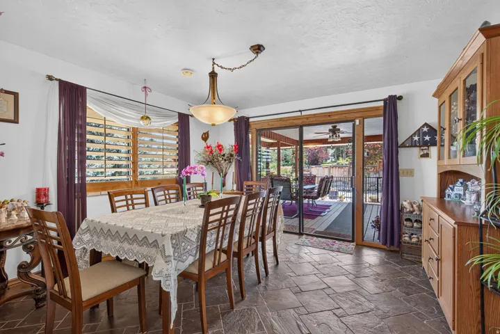 Spacious room featuring slate-style flooring, a large window with wooden shutters, and a sliding glass door providing direct access to an outdoor deck