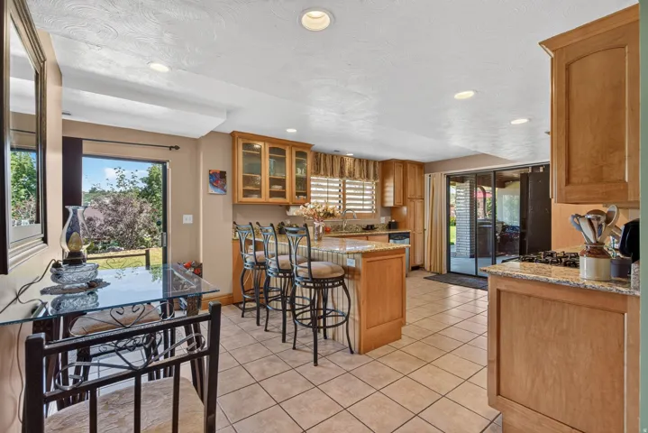 Kitchen featuring tile flooring, wood-finish cabinetry, a breakfast bar with seating, a gas cooktop, and sliding glass doors to outdoor spaces