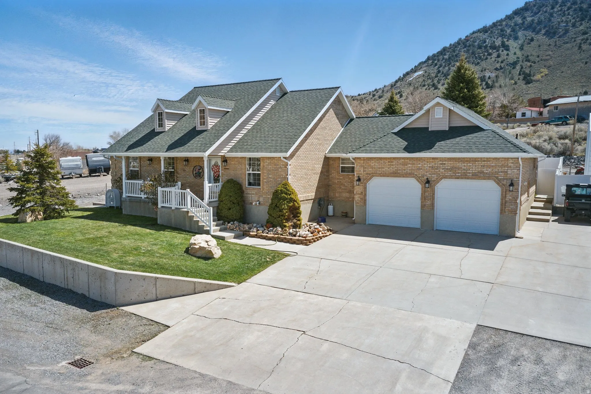 Brick exterior home featuring a two-car garage, dormer windows, covered front porch with white railing, a concrete driveway, and a manicured lawn