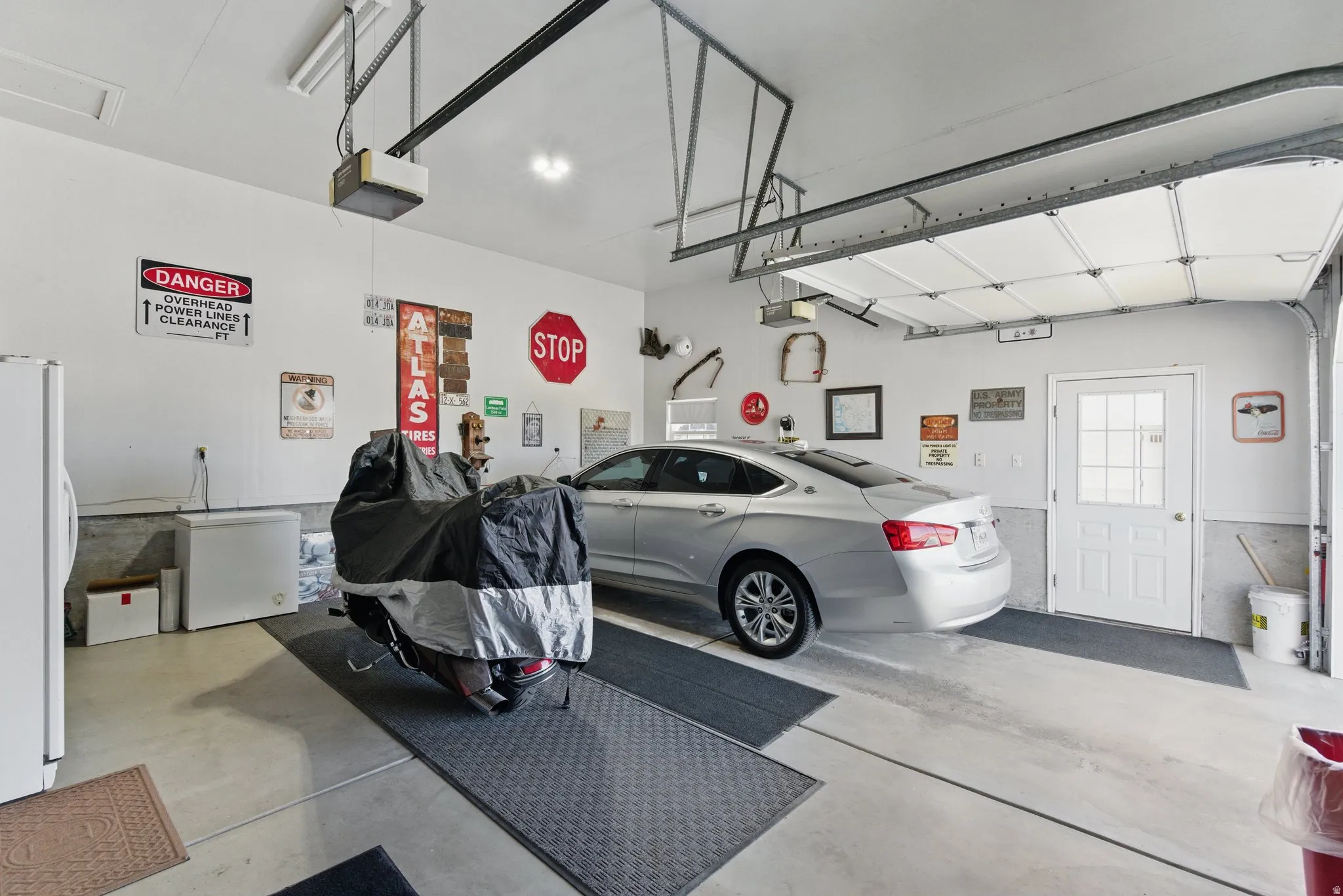 Spacious garage featuring concrete flooring, an overhead garage door, automatic garage door opener, and a white side entry door with lites
