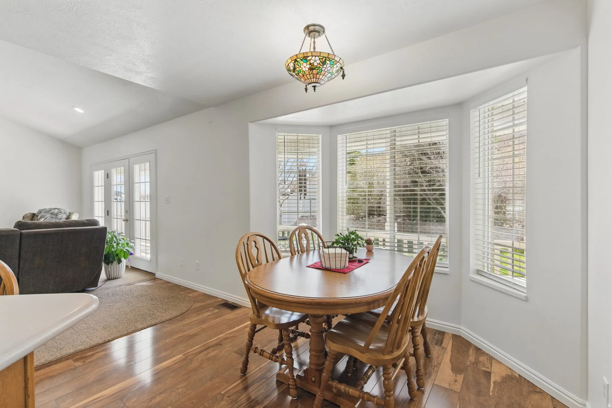 Bay window dining area featuring wood-finish flooring, a decorative stained-glass pendant light fixture, and white window blinds