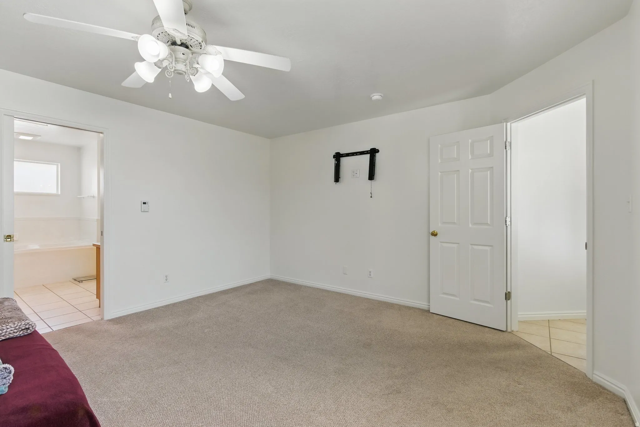 Carpeted room with white walls, a ceiling fan with integrated lighting, and a wall-mounted bracket