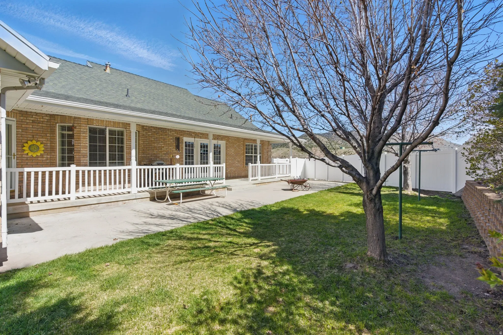 Expansive concrete patio bordered by white railings, featuring a brick exterior and a grey shingle roof