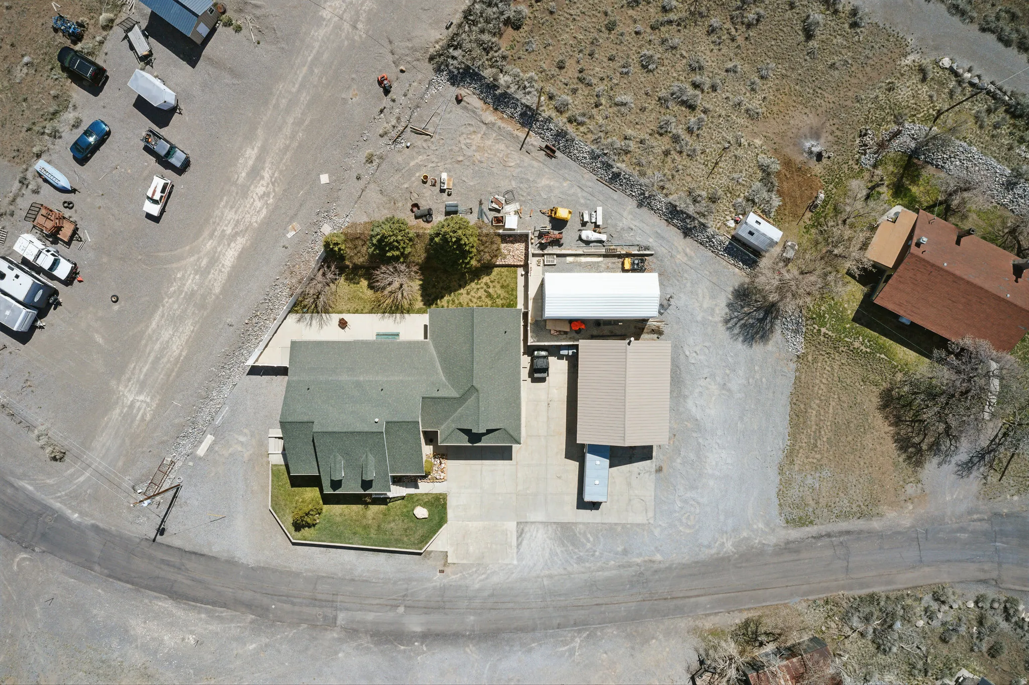 Aerial view showcasing a residential structure with a dark green roof, an expansive concrete driveway, and an attached covered carport