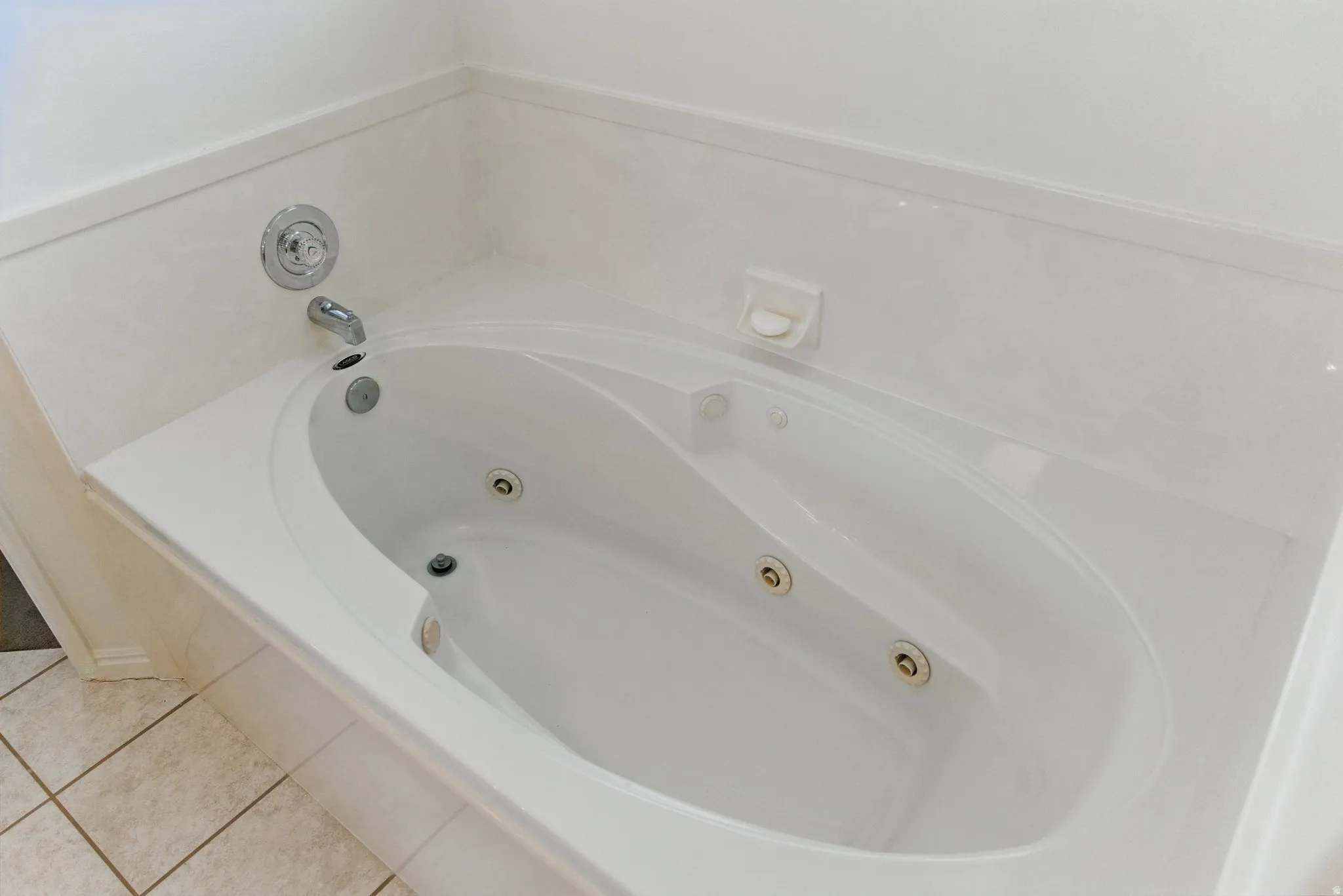 Corner soaking tub with integrated jets, chrome fixtures, and surrounding tile deck