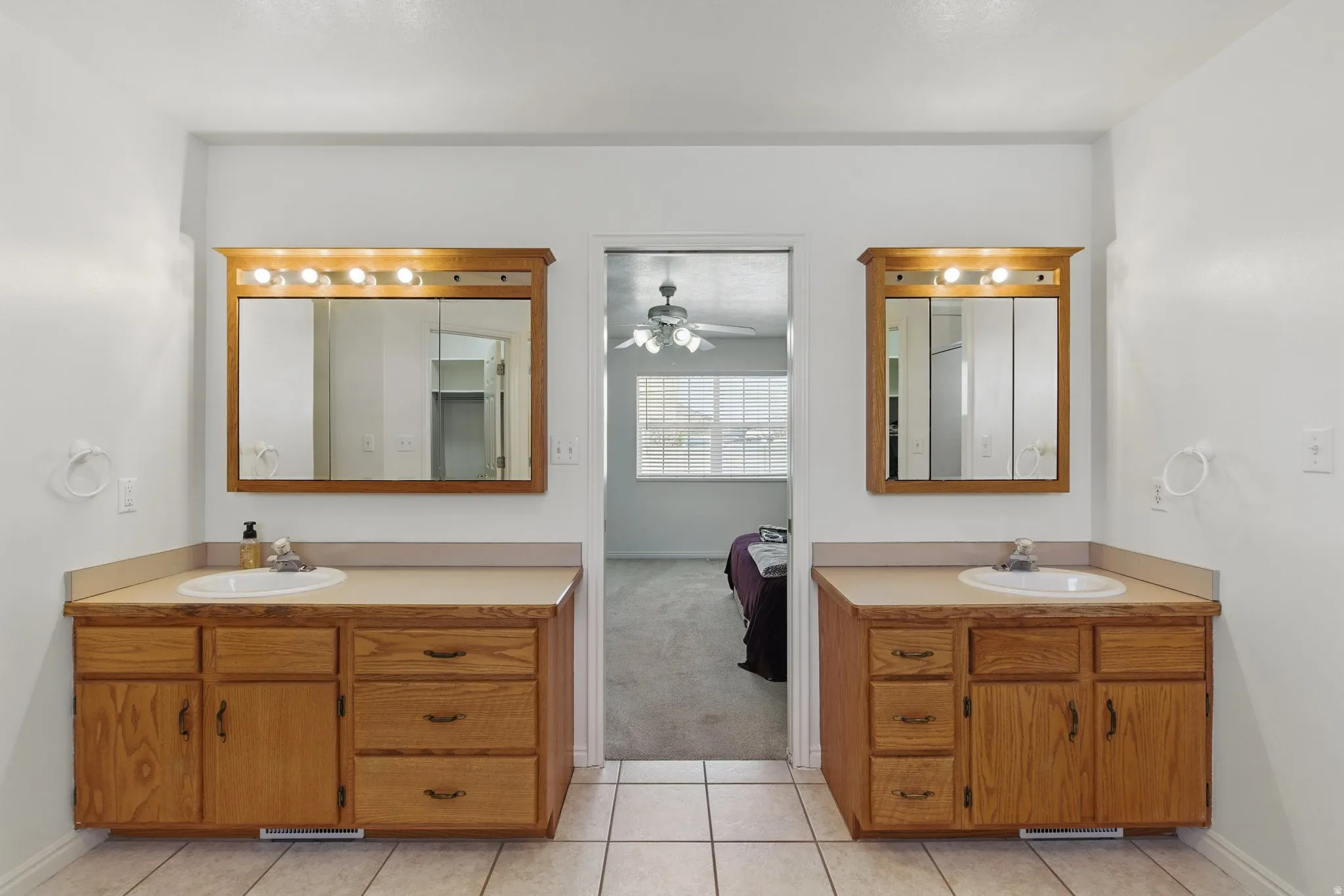 Dual vanity setup featuring light wood cabinetry with built-in storage, individual sinks, and overhead lighting fixtures