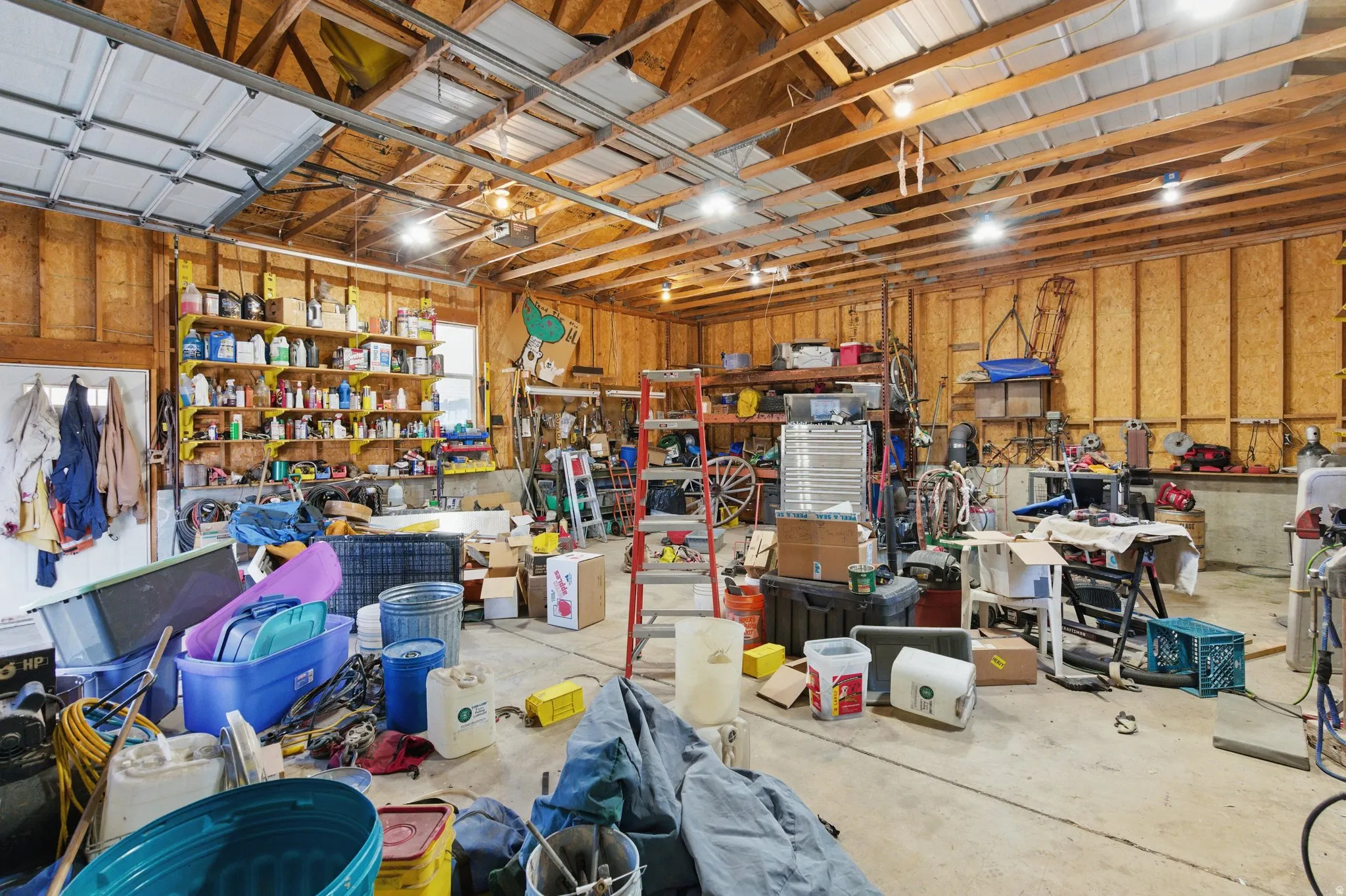 Spacious garage interior featuring exposed wood framing, multiple overhead lighting fixtures, and a concrete floor