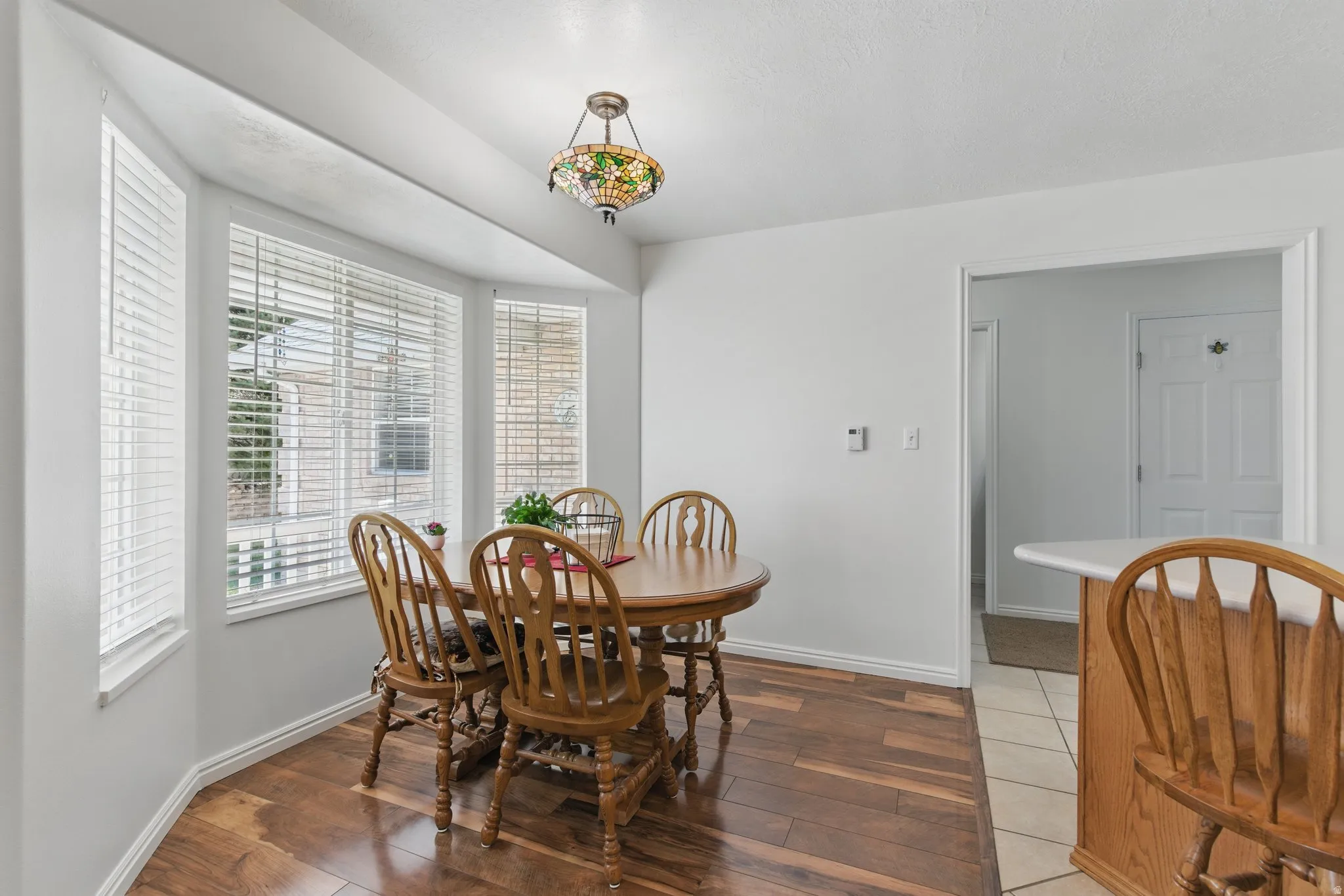 Bay window with white blinds and trim, wood-finish flooring, and a decorative pendant light fixture