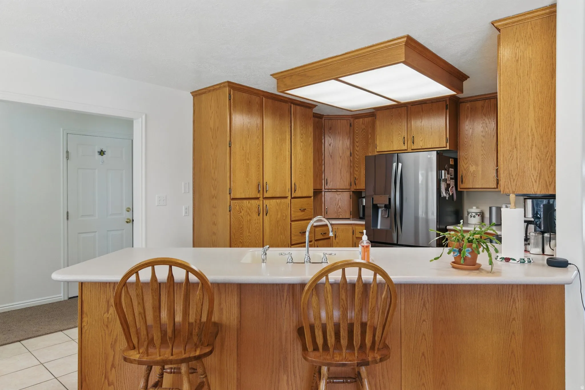 Kitchen featuring extensive wood cabinetry, a stainless steel refrigerator, and a light-toned countertop with an integrated sink and breakfast bar