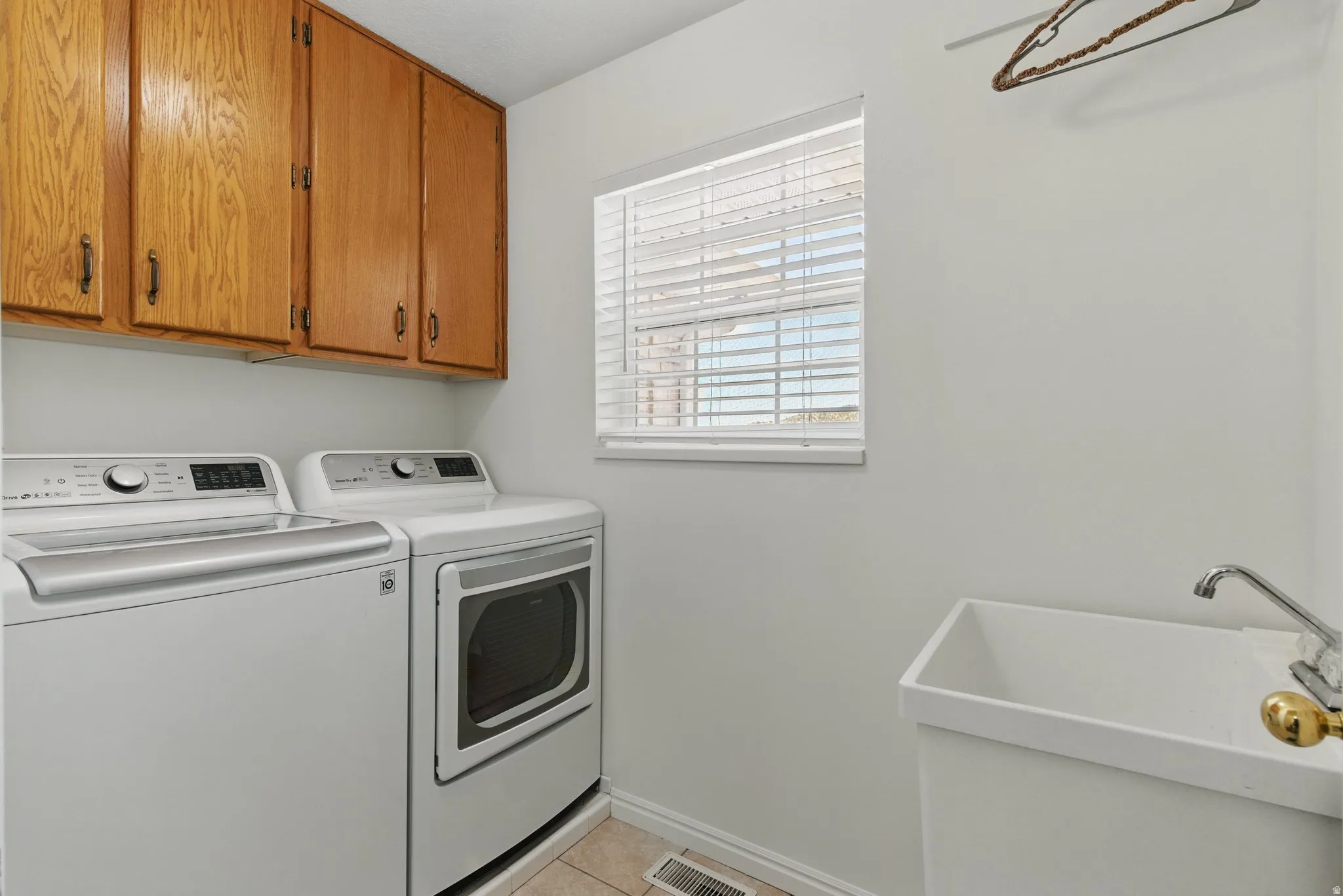 Laundry room featuring ample overhead cabinetry, utility sink with faucet, window with blinds, and tile flooring
