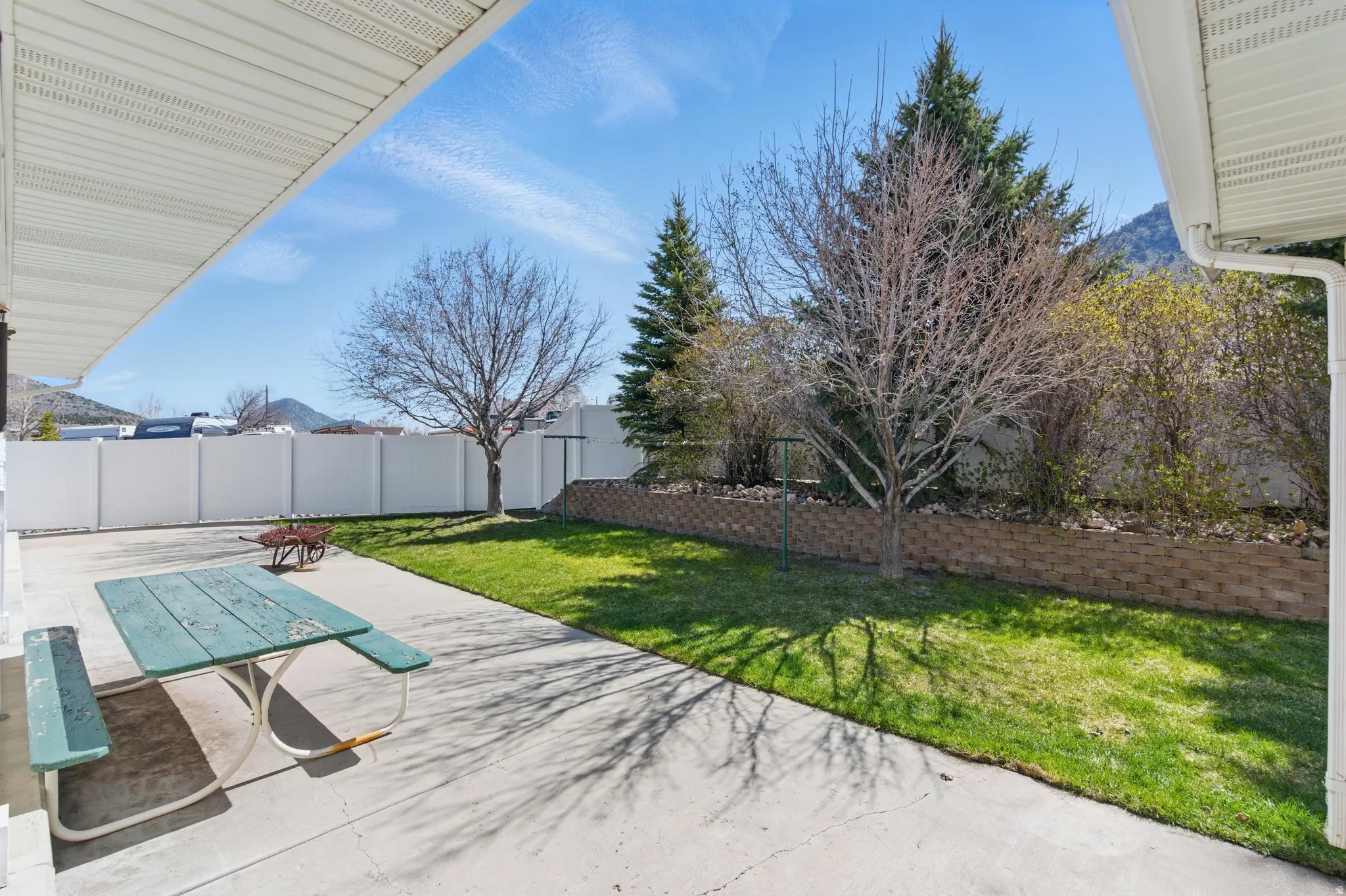 Spacious patio area with concrete surfacing, a manicured lawn, and mature trees