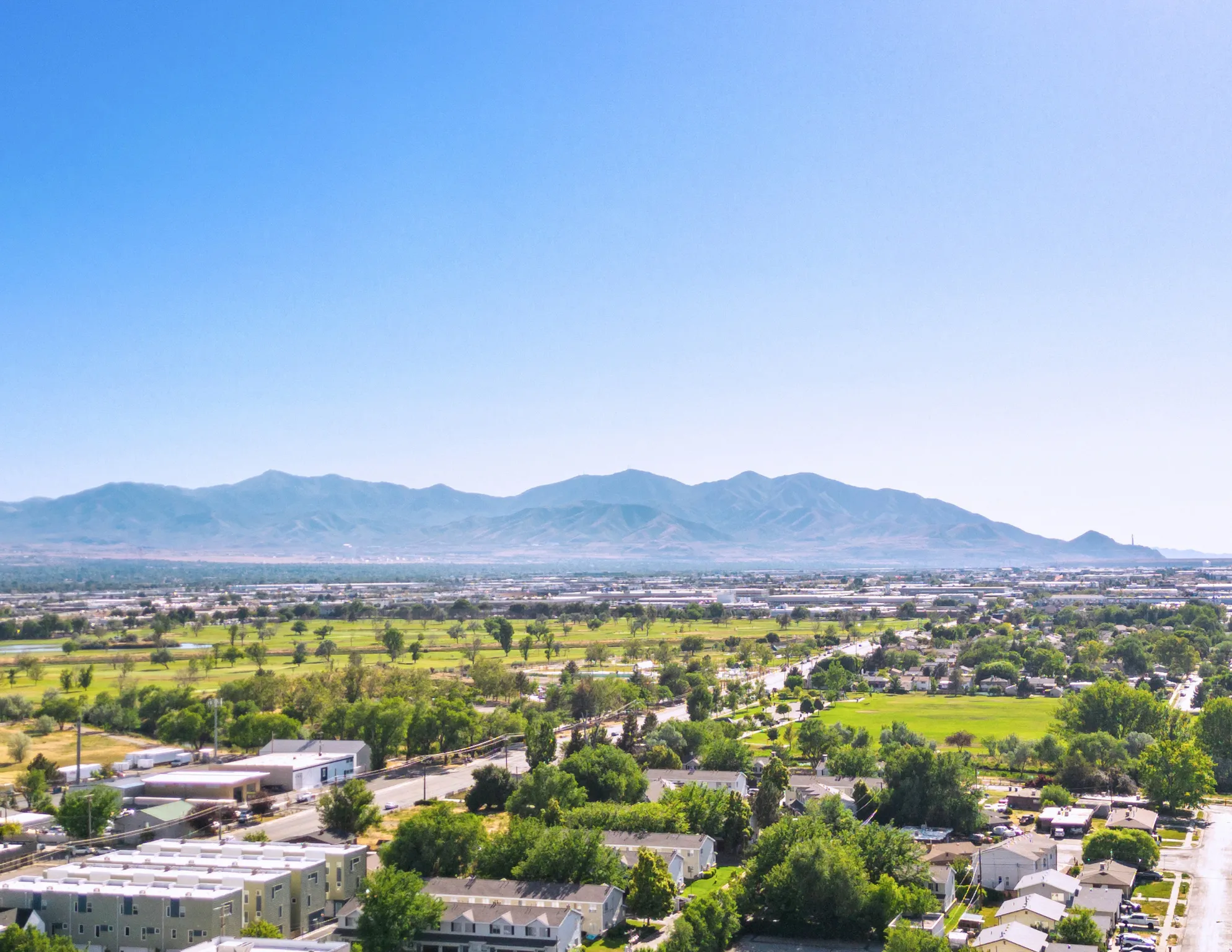 Expansive mountain backdrop with a vast green landscape featuring developed areas and residential structures