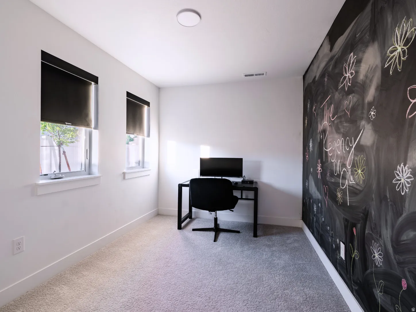 Light-filled room featuring two windows with blackout roller shades, a chalkboard accent wall, plush carpeting, and recessed ceiling lighting