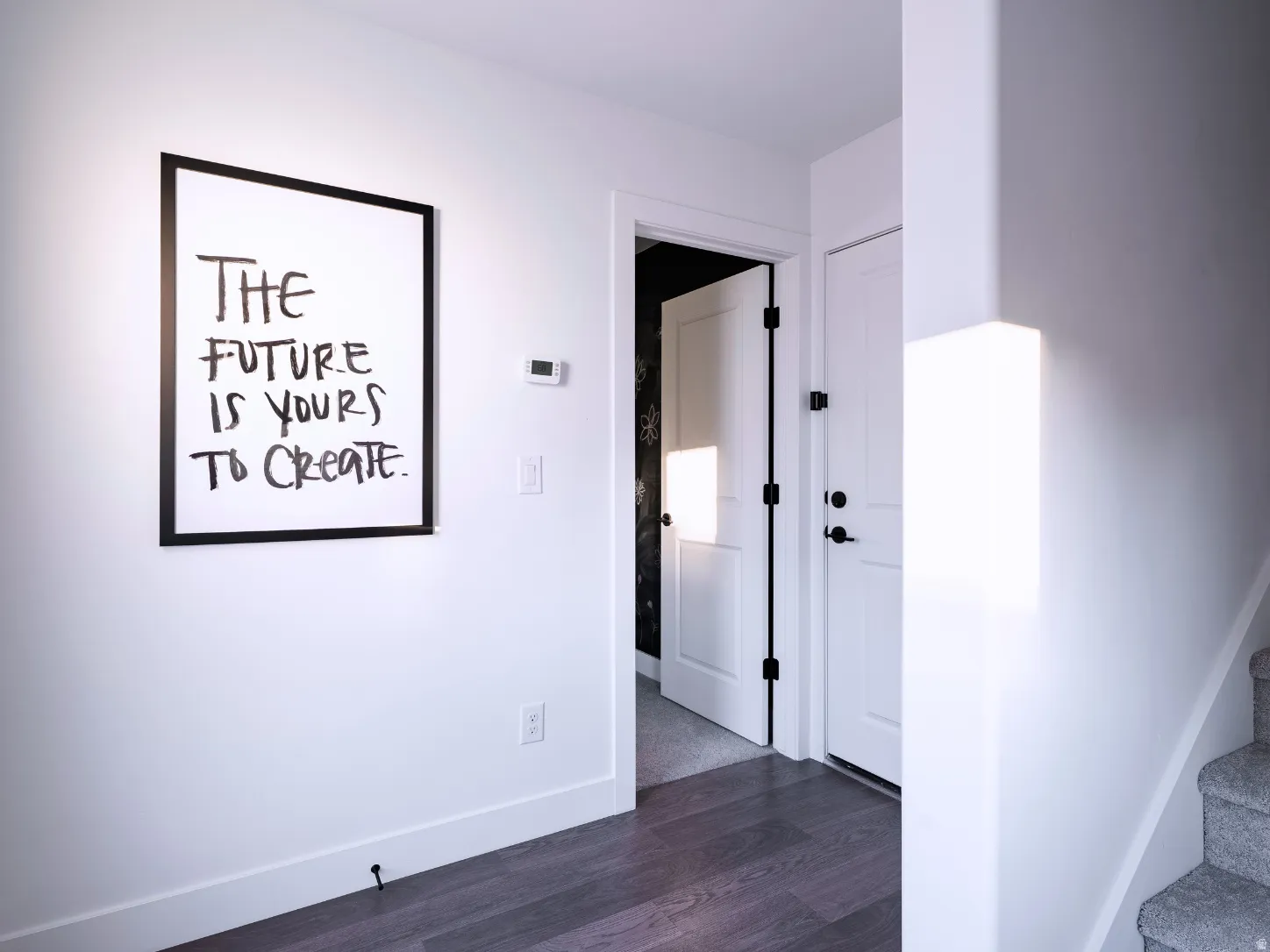 Modern entryway featuring dark wood-finish flooring, white paneled doors with matte black hardware, and a contemporary wall-mounted light fixture