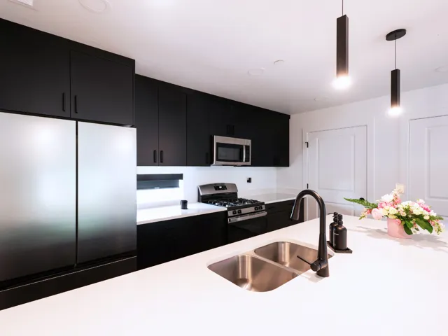 Contemporary kitchen featuring stainless steel appliances, black flat-panel cabinetry, white countertops, a dual basin sink with a matte black faucet, and pendant lighting