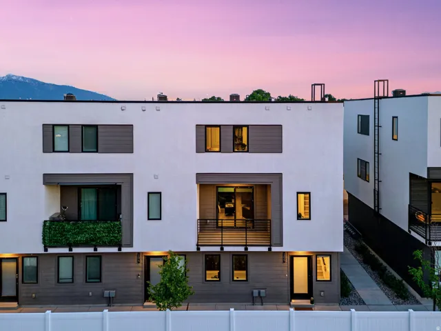 Modern architectural townhome featuring a private balcony with metal railings, a ground-level patio, and a white fence