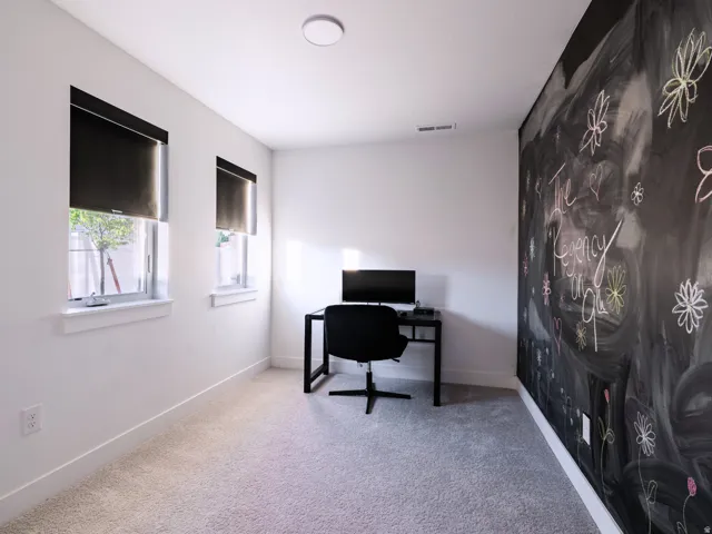 Light-filled room featuring two windows with blackout roller shades, a chalkboard accent wall, plush carpeting, and recessed ceiling lighting