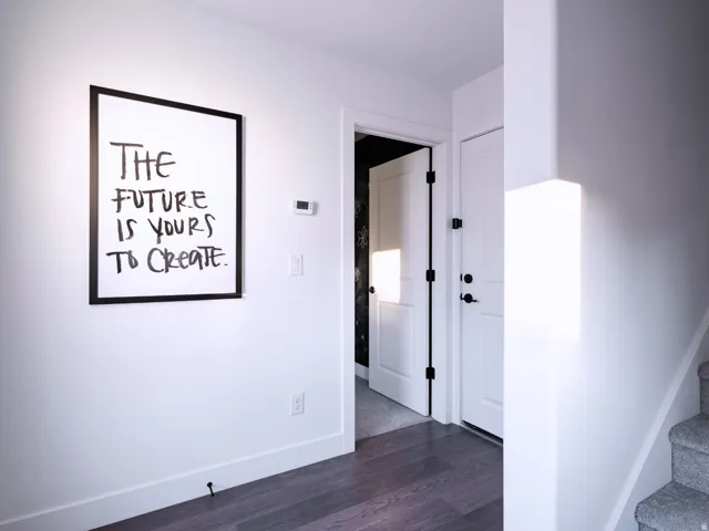 Modern entryway featuring dark wood-finish flooring, white paneled doors with matte black hardware, and a contemporary wall-mounted light fixture