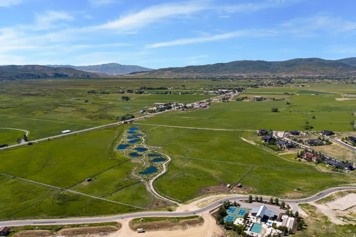 Expansive green landscape featuring multiple ponds, distant mountain ranges, and residential areas
