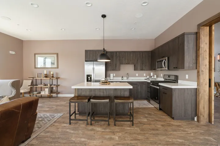 Open-concept kitchen featuring wood-finish flooring, white countertops, stainless steel appliances, and dark wood cabinetry