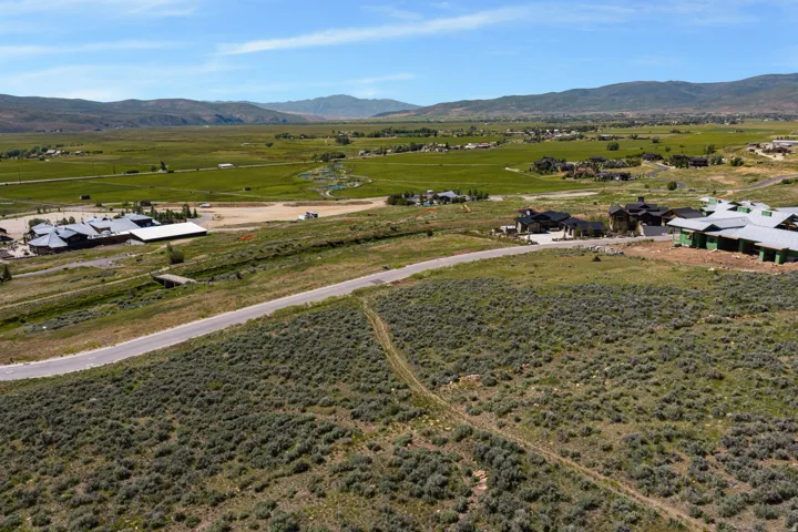 Expansive land parcel featuring natural shrubbery and a paved road, bordered by distant mountains