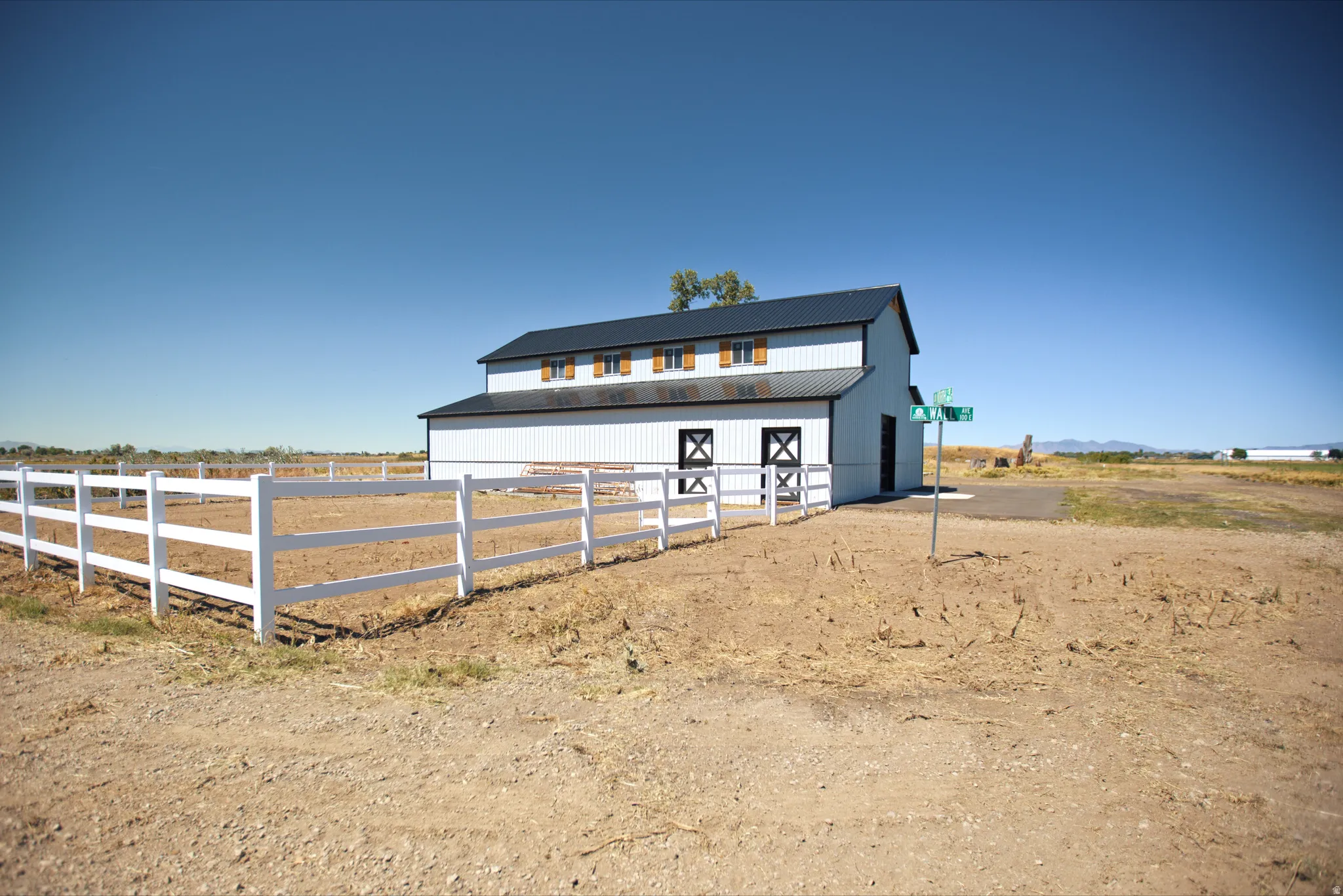 White barn structure with a dark metal roof and upper-level dormer windows featuring wood shutters