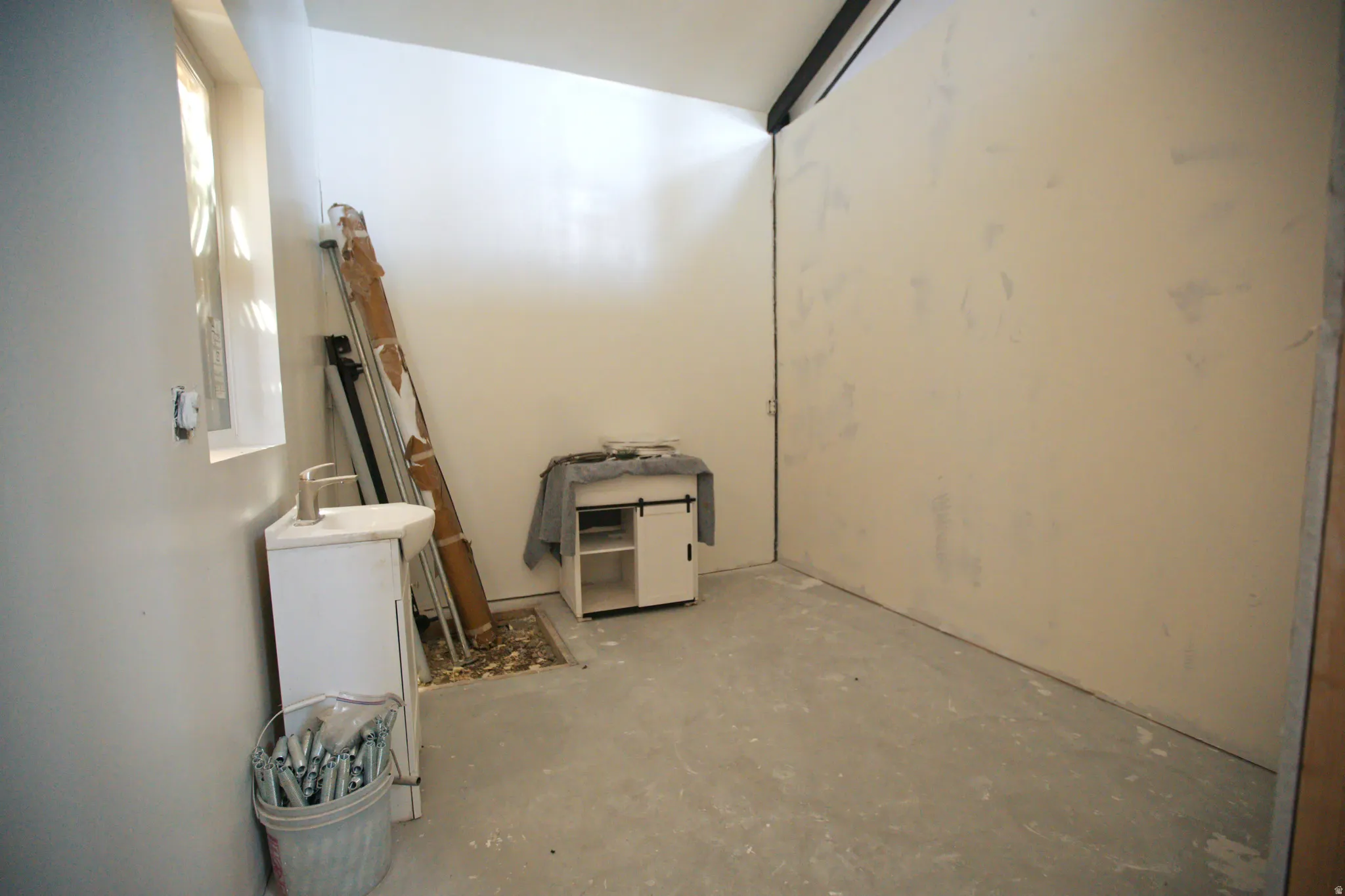 Compact room featuring a single window, white painted walls, and a concrete floor