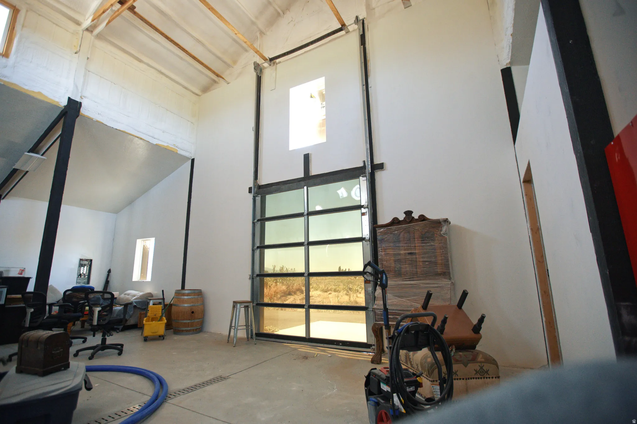 Expansive interior space featuring a full-glass roll-up door, high vaulted ceilings with exposed beams, and concrete flooring