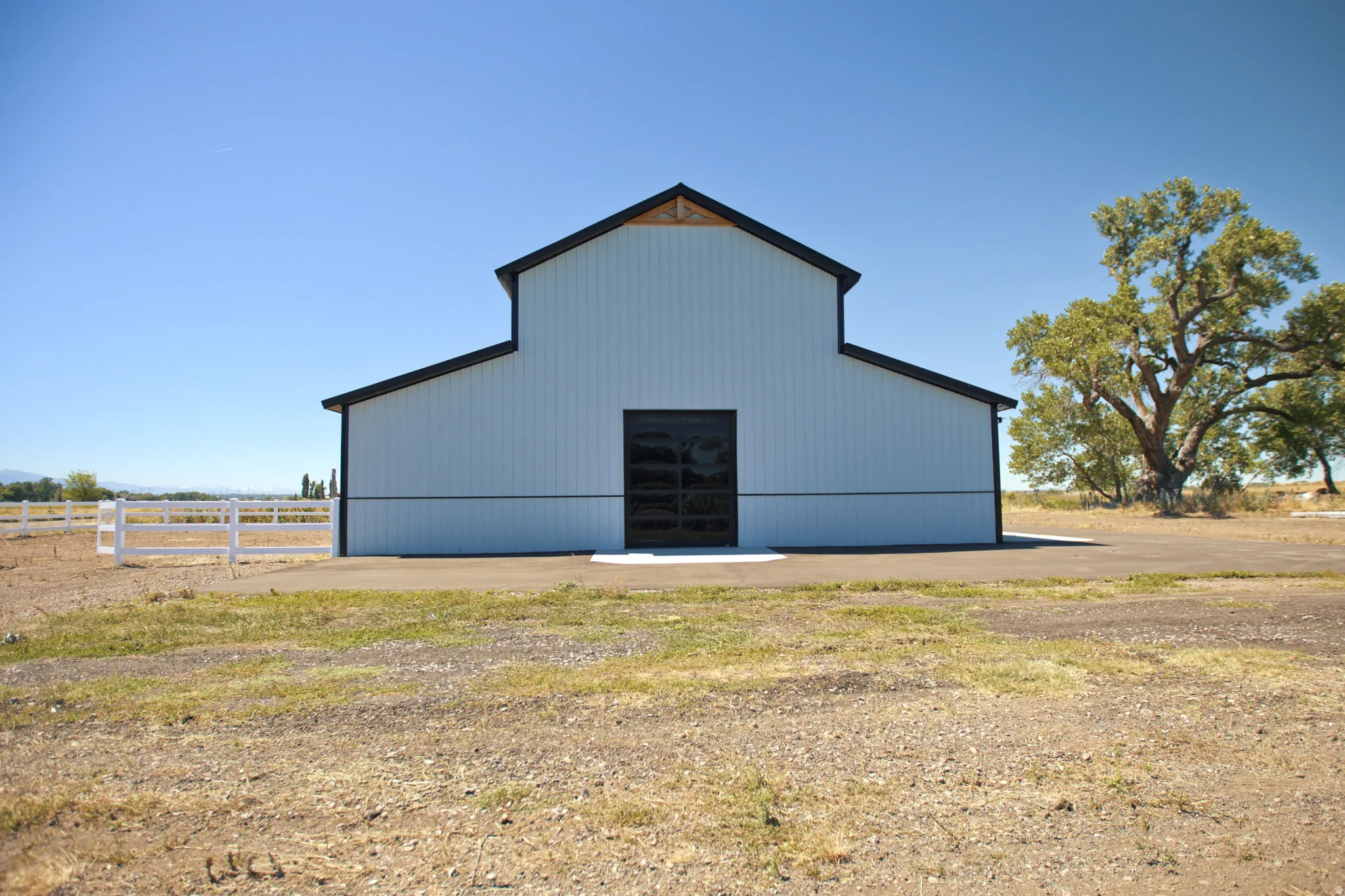 White-sided barn with black trim and a black garage door, set on a gravel and dirt lot