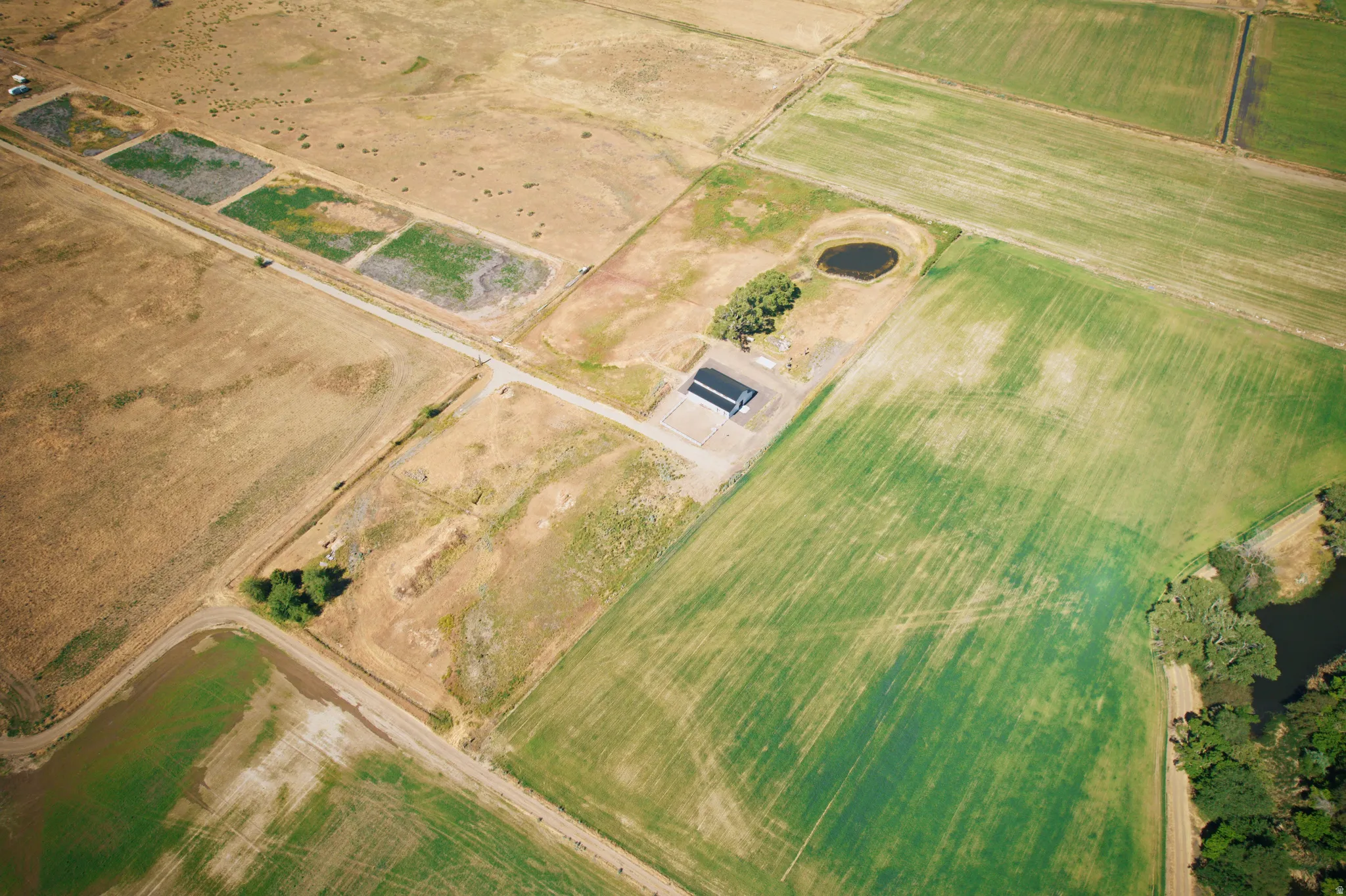 Expansive agricultural landscape featuring varied terrain, a large dark-roofed structure, and multiple water features including a pond and a river