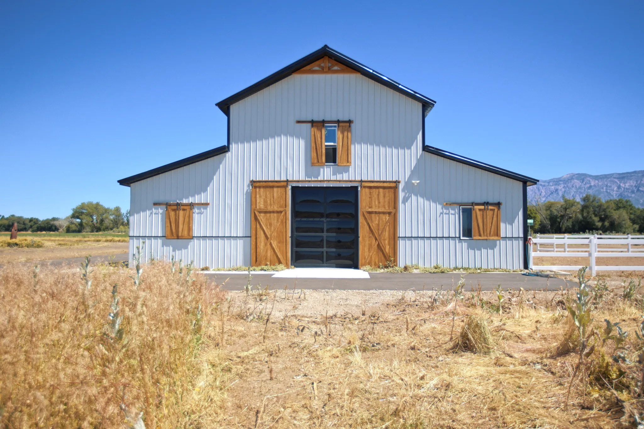 Modern barn-style structure featuring white corrugated metal siding, a black roof, and wood-finish sliding barn doors