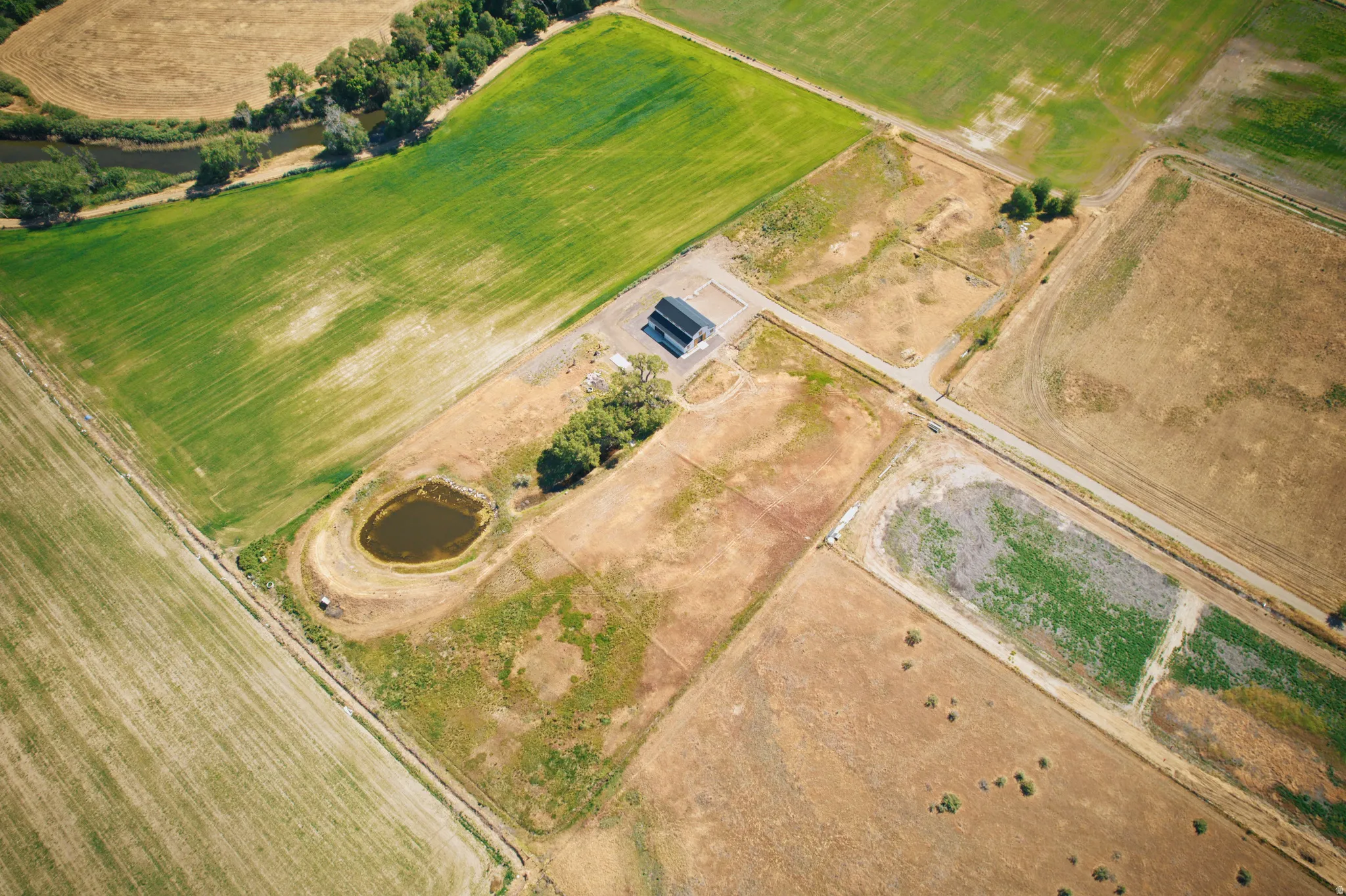 Aerial property overview featuring a single structure, surrounding fields, a small pond, and a meandering waterway